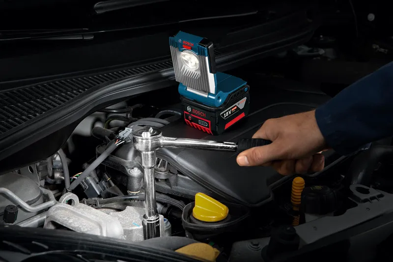 Henkilö korjaa auton moottoria jakoavaimella, jonka lähellä on akkutyövalo.