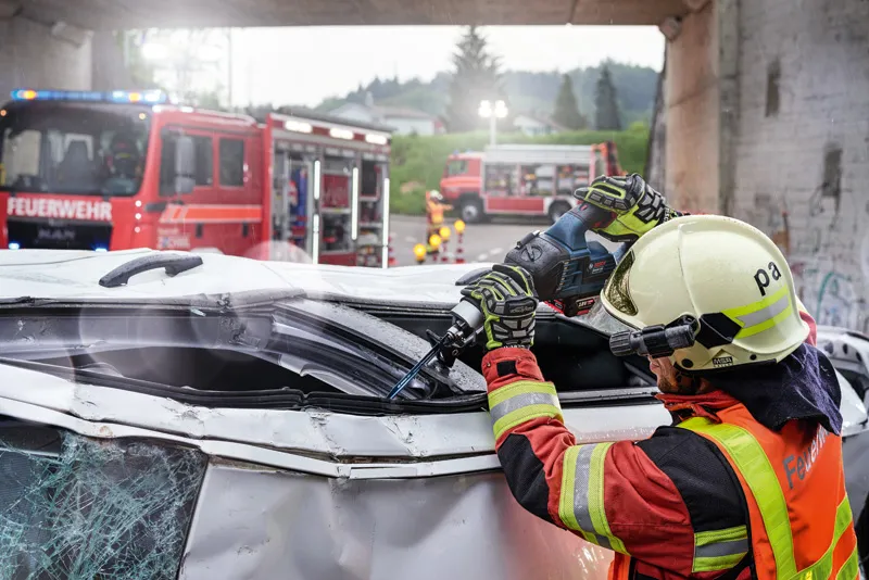 Turvavarusteita käyttävä henkilö leikkaa vaurioituneen ajoneuvon katon moottorisahalla.