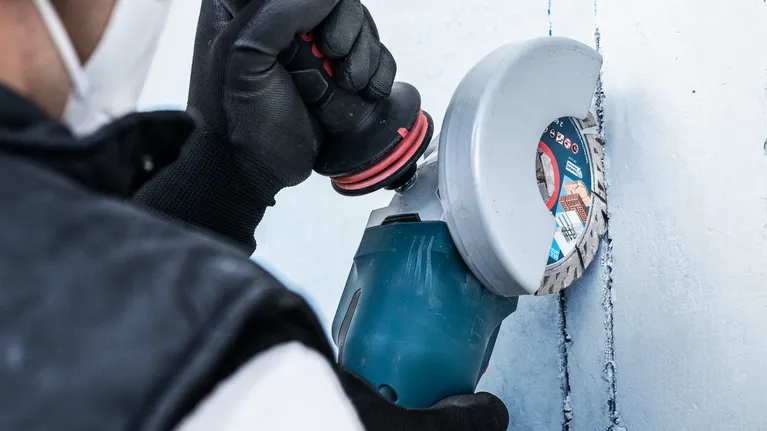 Turvavarusteita käyttävä henkilö tekee laikkaleikkurilla uria seinään.