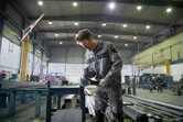 Turvavarusteita käyttävä henkilö hioo metallia, kipinät sinkoilevat suuressa teollisuusverstaassa.