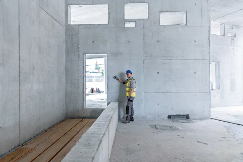 Turvavarusteita käyttävä henkilö käyttää lasermittauslaitetta betoniseinää vasten.