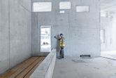 Turvavarusteita käyttävä henkilö käyttää lasermittauslaitetta betoniseinää vasten.