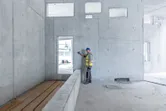 Turvavarusteita käyttävä henkilö käyttää lasermittauslaitetta betoniseinää vasten.