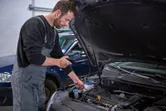 Henkilö tarkastaa auton moottoria tarkastuskameralla autotallissa.
