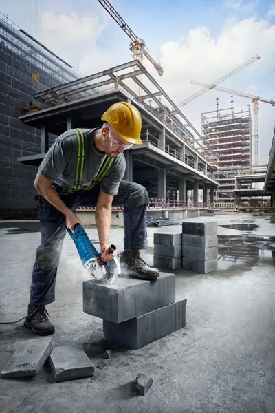 Turvavarusteita käyttävä henkilö leikkaa betonilohkoja rakennustyömaalla.