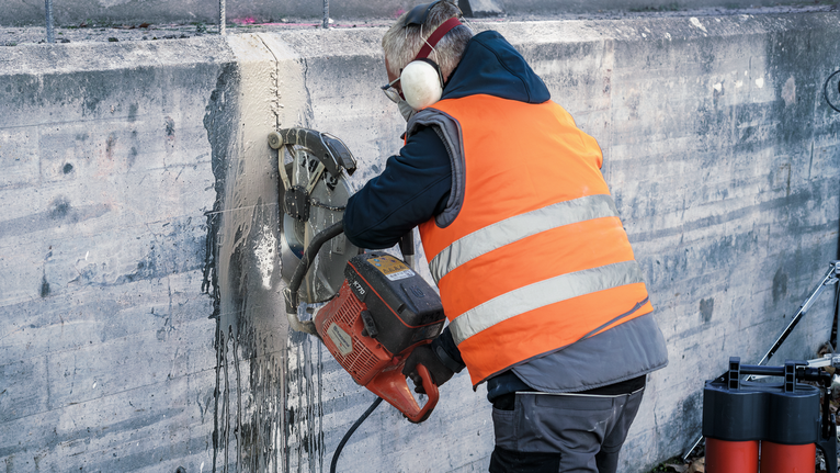 Turvavarusteita käyttävä henkilö leikkaa betoniseinän läpi moottorisahalla.