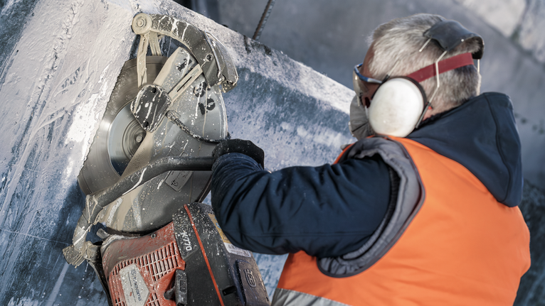 Turvavarusteita käyttävä henkilö sahaa pyörösahalla suurta betonilohkoa.