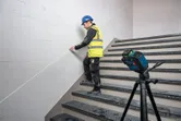 Turvavarusteita käyttävä henkilö merkitsee portaiden seinää laservaaituslaitteella.