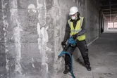 Turvavarusteita käyttävä henkilö käyttää purkuvasaraa betoniseinään.