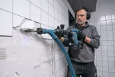 Turvavarusteita käyttävä henkilö poistaa seinälaattoja sähköporakoneella.