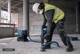 Turvavarusteita käyttävä henkilö käyttää pölynimulaitetta poratessaan betonia.