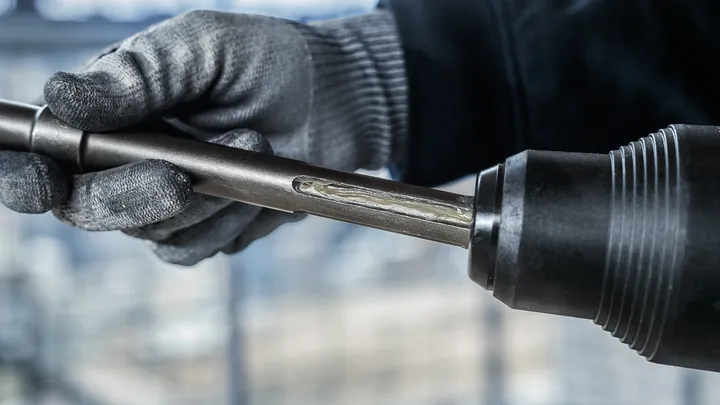 Turvavarusteita käyttävä henkilö työntää metallisen poranterän sähkötyökaluun.