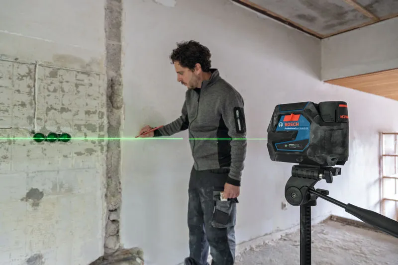 Henkilö merkitsee seinää laserilla ja heijastaa vihreän vaakasuoran viivan.