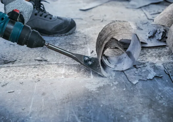 Turvavarusteita käyttävä henkilö käyttää sähkötyökalua lattiamateriaalin poistamiseen.