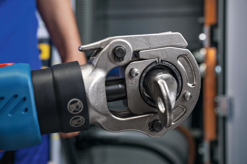 Turvavarusteita käyttävä henkilö käyttää akkukäyttöistä hydraulista puristustyökalua paneelin edessä.