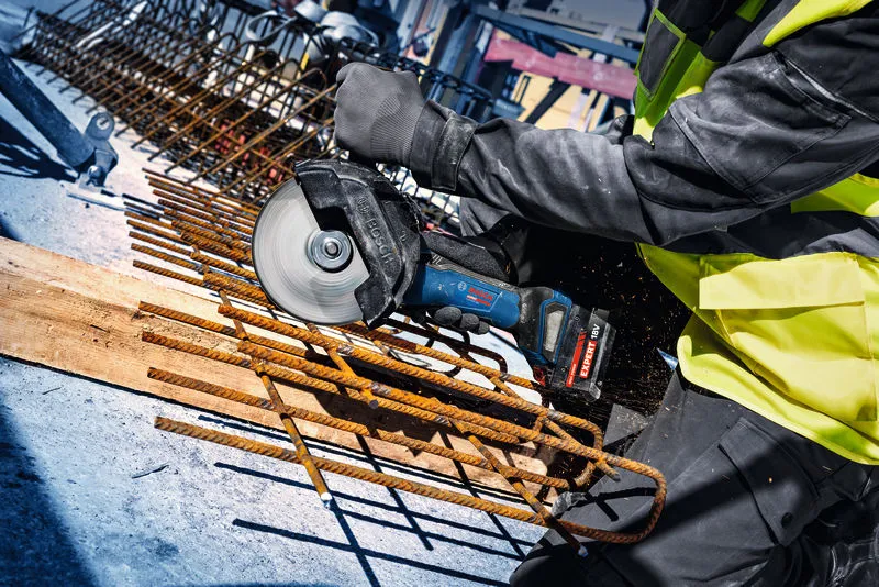 Turvavarusteita käyttävä henkilö leikkaa terästä akkukulmahiomakoneella.