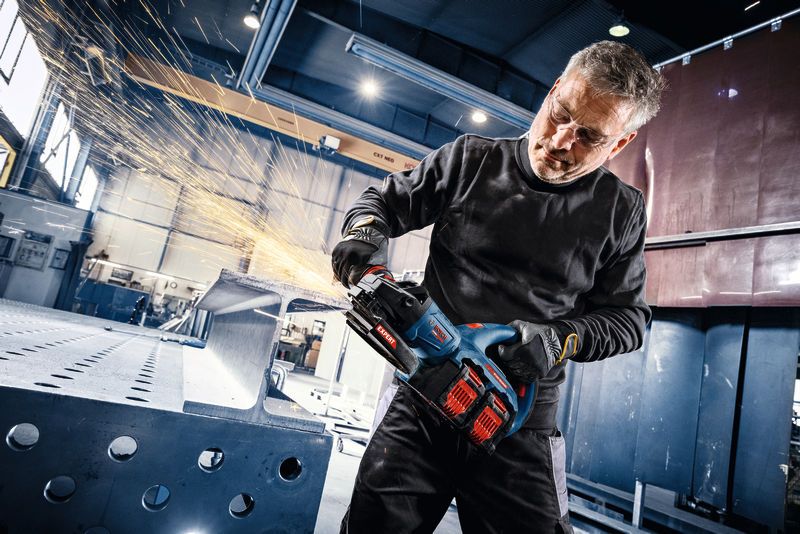 Turvavarusteita käyttävä henkilö hioo teräspalkkia akkukulmahiomakoneella.