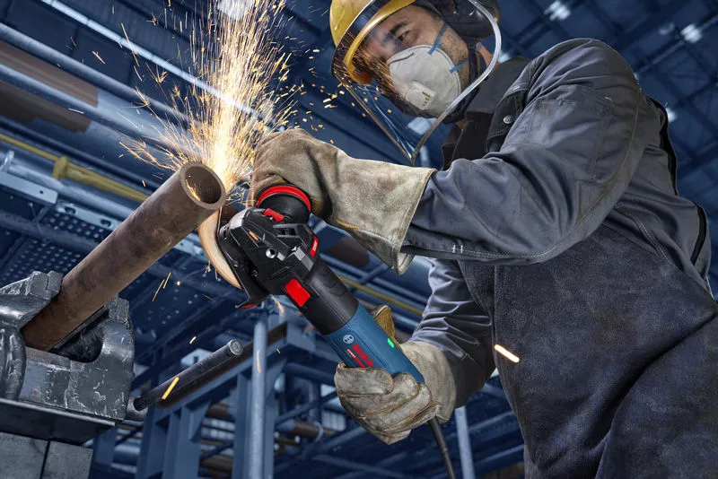 Turvavarusteita käyttävä henkilö hioo metalliputkea, jolloin syntyy kipinöitä.