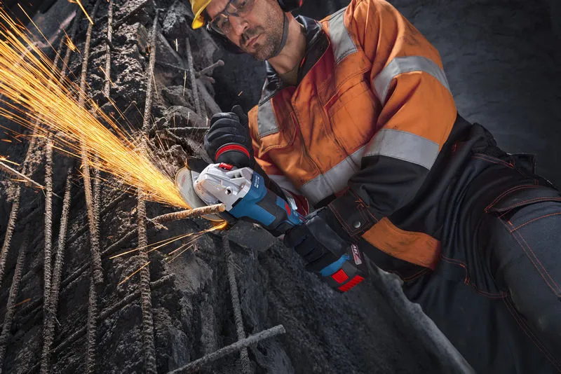 Turvavarusteita käyttävä työntekijä leikkaa metalliteräspalkkia kulmahiomakoneella.