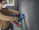 Turvavarusteita käyttävä henkilö leikkaa kulmahiomakoneella uran betoniseinään.