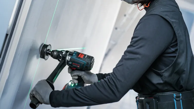 Turvavarusteita käyttävä henkilö poraa seinään sähkötyökalulla.