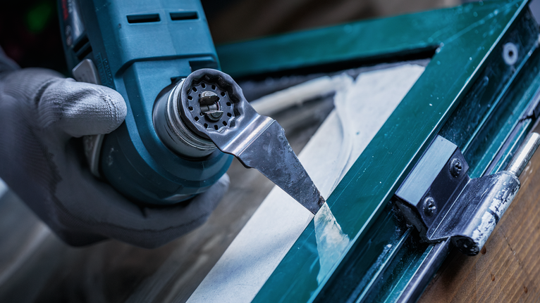 Turvavarusteita käyttävä henkilö poistaa ikkunakittiä monitoimityökalulla.