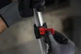 Turvavarusteita käyttävä henkilö säätää punaista puristinta metallitangossa.