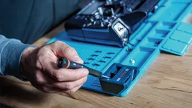 Henkilö käyttää ruuvimeisseliä elektroniseen komponenttiin työasemalla.