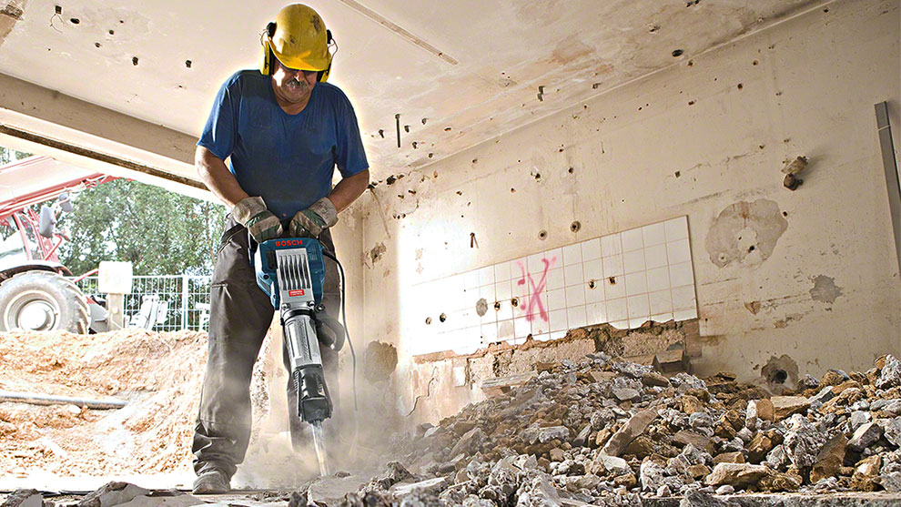 Mies käyttää Bosch-työkalua purkamistyössä, ympärillä on kivijätettä.