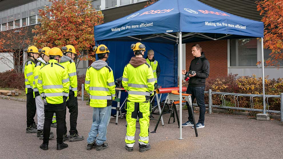 Bosch-teltta, keltaisia vaatteita päällä olevia henkilöitä, opetusvälineet näkyvät.