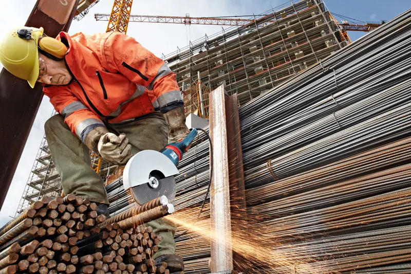 Une personne portant un équipement de sécurité coupe des tiges d'acier avec une meuleuse d'angle sur un chantier de construction.