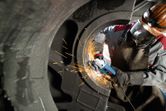 Une personne portant un équipement de sécurité broie du métal à l’intérieur d’un grand composant industriel.