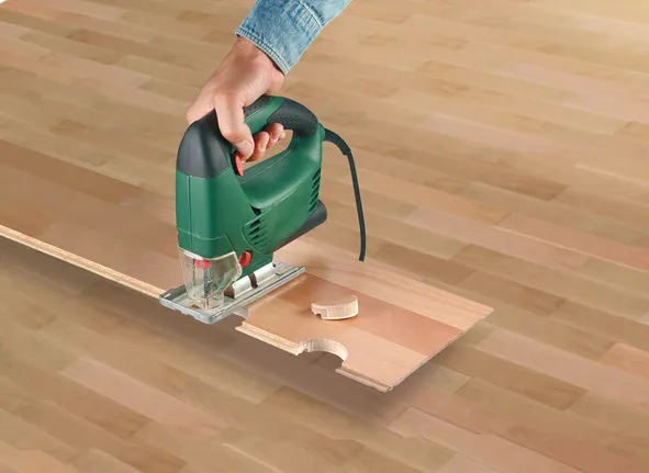 Une personne utilise une scie sauteuse pour découper une encoche circulaire dans une planche de bois.