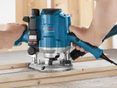 Une personne utilise une défonceuse bleue pour façonner le bord d'une planche de bois.
