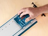 Une personne utilise un accessoire système bleu sur un rail métallique posé sur une surface en bois.