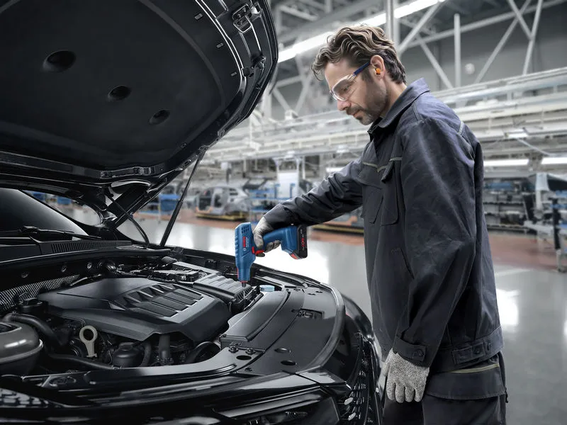 Une personne portant un équipement de sécurité utilise un pistolet thermique sur une chaîne de montage automobile.