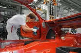 Une personne portant un équipement de sécurité utilise une perceuse sans fil pour assembler une porte de voiture dans une usine.