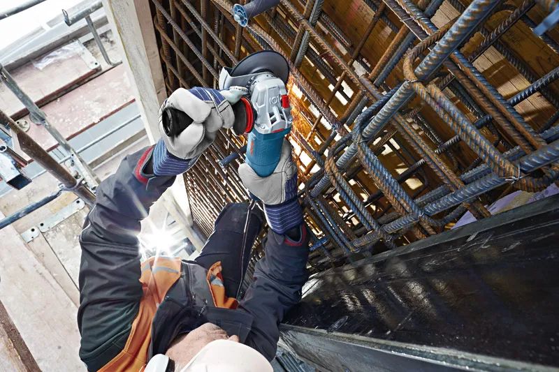 Une personne portant un équipement de sécurité broie des barres d'armature métalliques sur un chantier de construction.