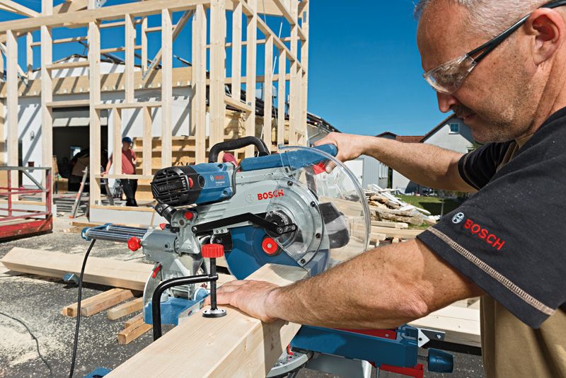 Une personne portant un équipement de sécurité coupe du bois avec une scie à onglet coulissante sur un chantier de construction.