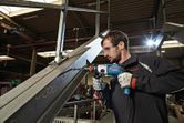 Une personne portant un équipement de sécurité utilise une perceuse pour faire un trou dans une poutre métallique.