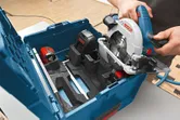Une personne place une scie circulaire sans fil dans un étui de transport avec batterie et chargeur.