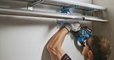 Une personne portant un équipement de sécurité utilise une perceuse électrique pour monter des tuyaux métalliques sur un mur.