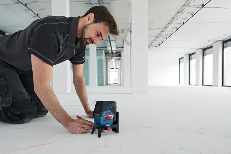 Une personne utilise un outil de nivellement laser avec un accessoire pour marquer des lignes sur un sol de construction.