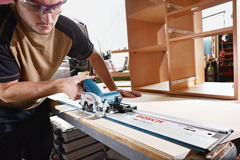 Une personne portant un équipement de sécurité utilise une scie circulaire sans fil pour couper du bois dans un atelier.