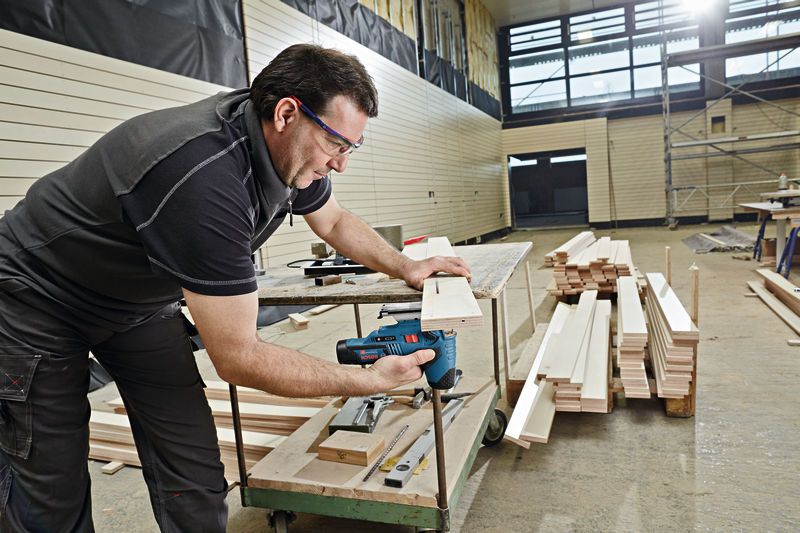 Une personne portant un équipement de sécurité coupe du bois avec une scie sauteuse sans fil dans un atelier.