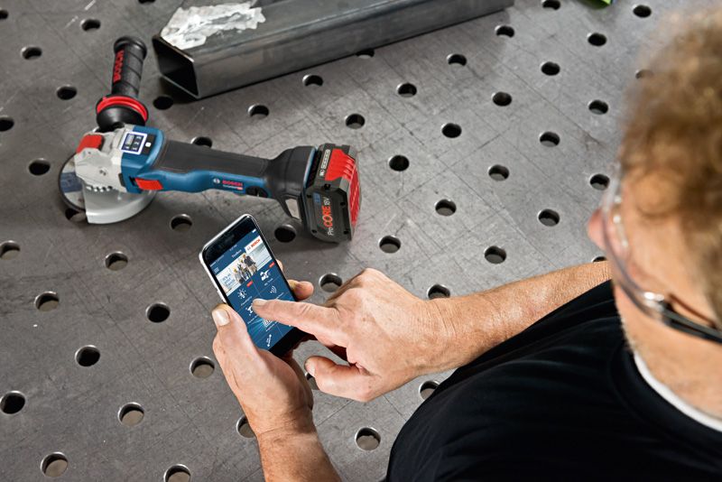 Une personne portant un équipement de sécurité utilise un smartphone pour contrôler une meuleuse d’angle sans fil.