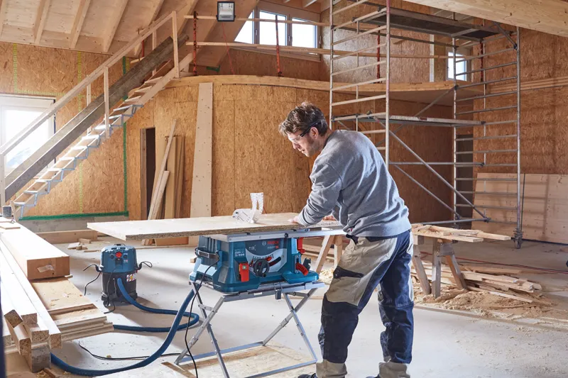 Une personne utilise une scie circulaire pour couper du bois dans un bâtiment partiellement construit.