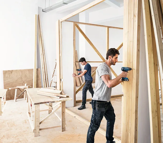 Deux hommes construisent un mur en bois.