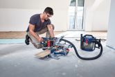 Une personne portant un équipement de sécurité coupe un parquet avec une scie à onglets sans fil.
