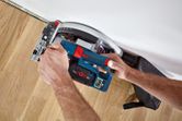 Une personne utilise une scie circulaire sans fil pour couper un parquet près d’un mur.